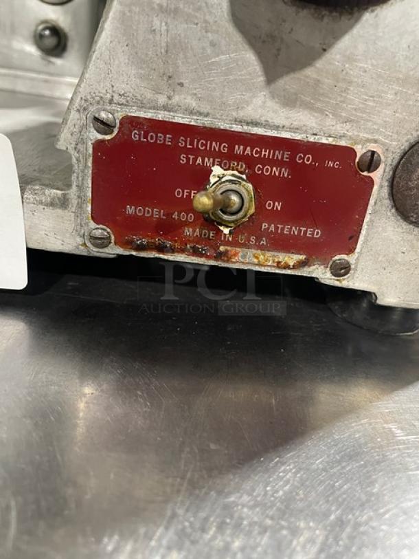 Globe Model 400 meat slicer, heavy-duty, electric-powered. Features control switch, label indicating "Made in USA." On legs.
