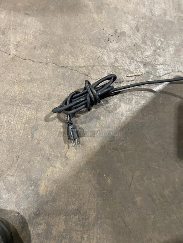 A black power cord coiled on a concrete floor.