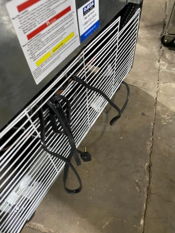 Ojeda FMH27 commercial refrigerator back view, showing power cables and poly-coated wired rack. Model and warning labels visible.