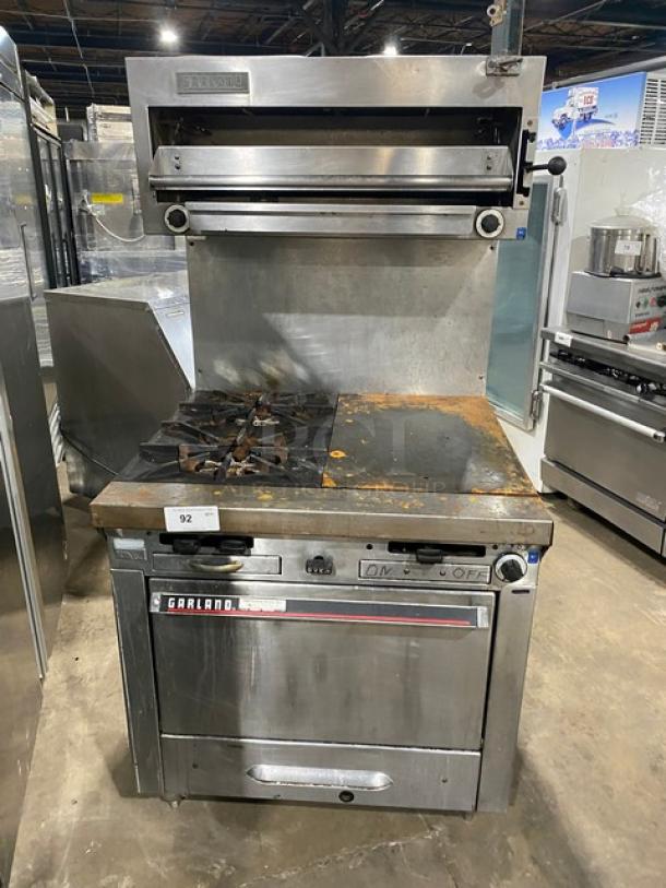 Garland stainless steel 2-burner, flat-plate range with oven, backsplash, salamander broiler, and wired rack, on legs.
