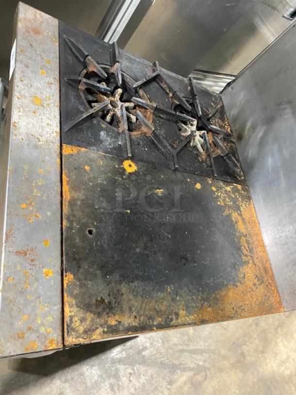 Garland commercial stainless steel 2 burner/flat plate range and oven combo with backsplash, salamander broiler, wired oven rack, on legs. Visible wear and rust on surface.
