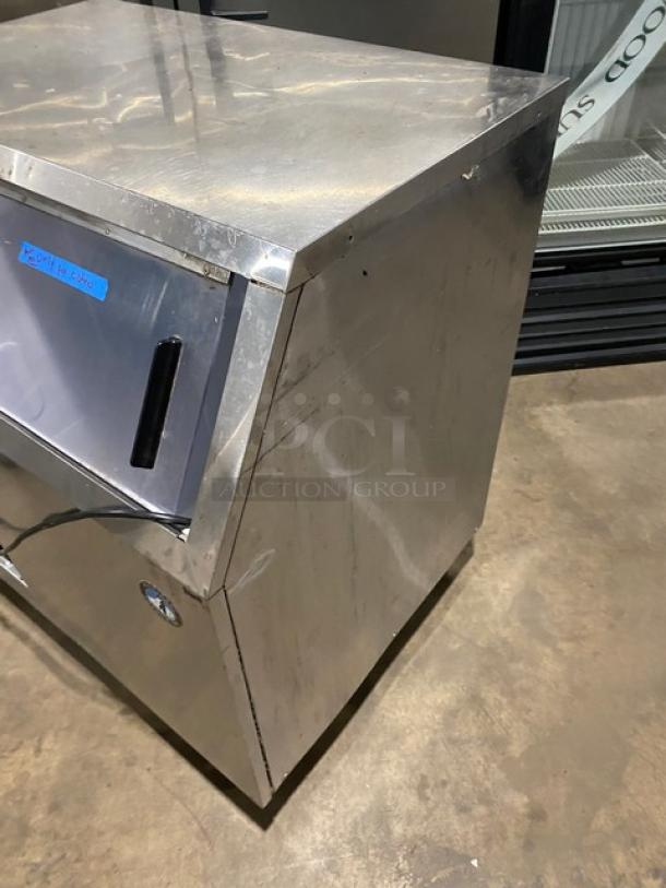 Hoshizaki stainless steel undercounter ice machine with sliding door, on legs. Visible scratches, electric powered, label present.