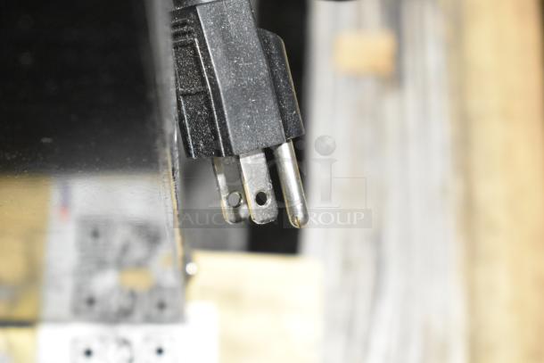 Black plug with three prongs, close-up view against a blurred background.