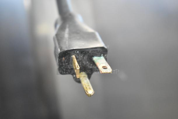 Close-up of a standard black electrical plug with visible metal prongs, slightly oxidized.