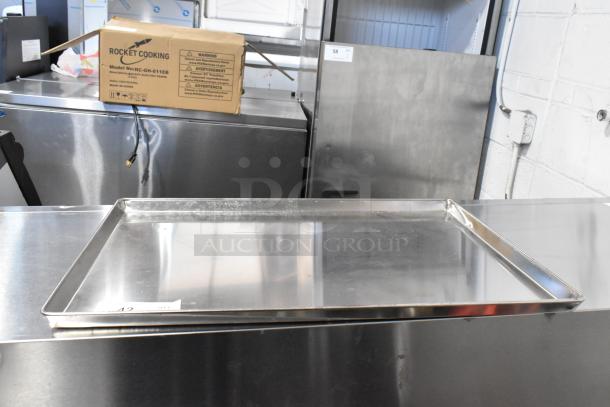 24 metal full-size baking pans, new condition, durable stainless steel, stackable. Includes box labeled "Rocket Cooking."