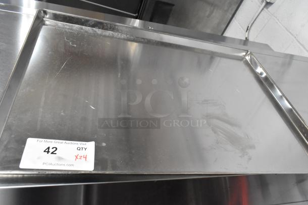 Set of 24 metal full-size baking pans, slightly used, shiny finish. Visible auction tag with quantity and bid details.