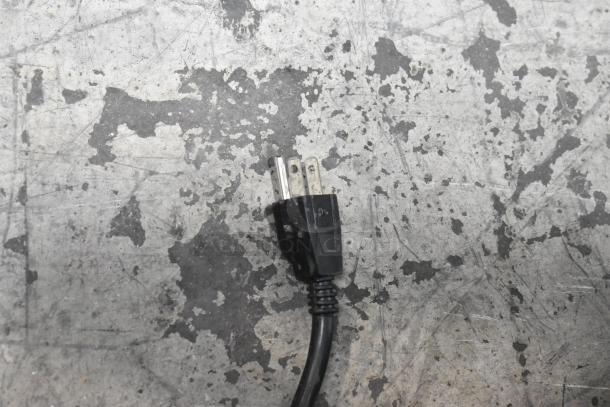 Close-up of a black electrical plug on a scratched metal surface.