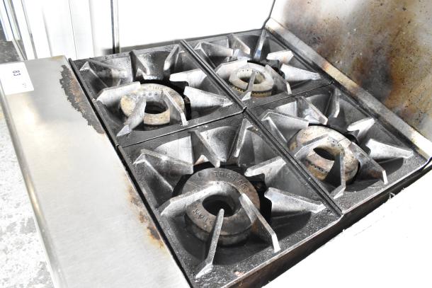 Tri-Star stainless steel commercial 4 burner gas range with oven, overshelf, and backsplash, showing signs of use.