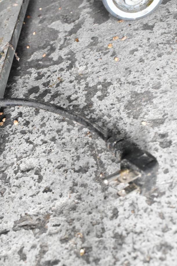 A black electrical plug on a concrete surface, with part of a wheel visible in the background.