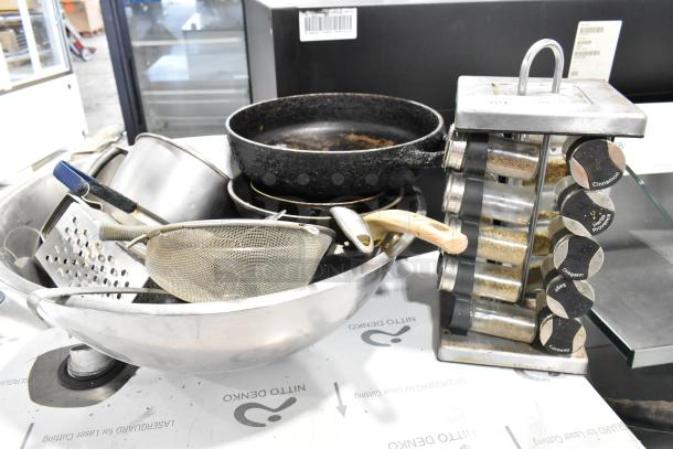 Lot of various kitchen items including spice rack, cast iron skillet, graters, metal bowl, and strainer in used condition.
