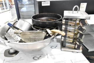 Lot of various kitchen items including spice rack, cast iron skillet, graters, metal bowl, and strainer in used condition.