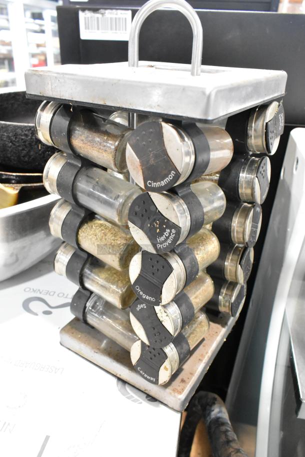 Rotating spice rack with labeled glass jars, including cinnamon and oregano. Visible wear and metal top handle. Skillets and metal bowl in background.