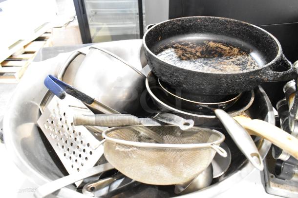 Lot of kitchen items including cast iron skillet, metal bowls, wire strainer, grater; all in used condition.