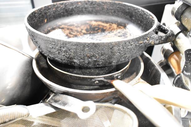 Lot of various kitchen items including spice rack, iron skillets with worn texture, and metal bowl stacked together.