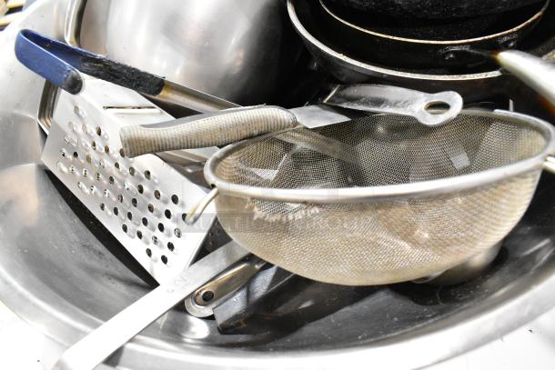 Lot of kitchen items including spice rack, skillets, metal bowl, grater, and strainer. Mixed materials, used condition.
