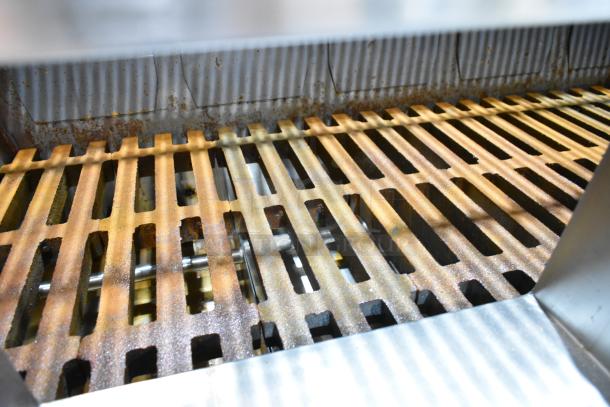 Champion Tuff 782TG60 stainless steel 60" wood burning grill, features rusted grates and corrugated backdrop, showing some wear.