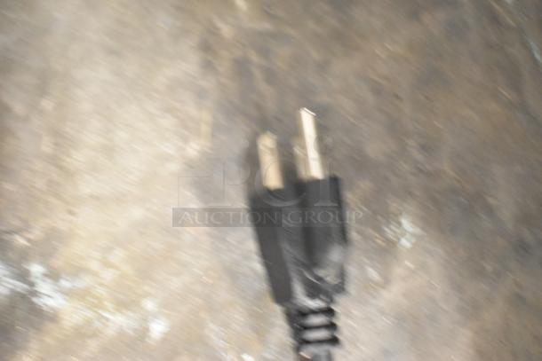 Blurred image of an electrical plug against a textured background. No other discernible details.