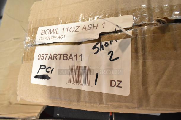 Cardboard box with label showing "957ARTBA11" and "BOWL 11OZ ASH 1 DZ ARTEFACT," indicating new porcelain bowls. Box is sealed with tape.
