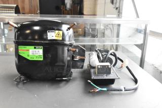 Brand new Secop SCE21CNLX motor, 115V, 1 phase, with visible scratch and dent. Labels show model and phase details.