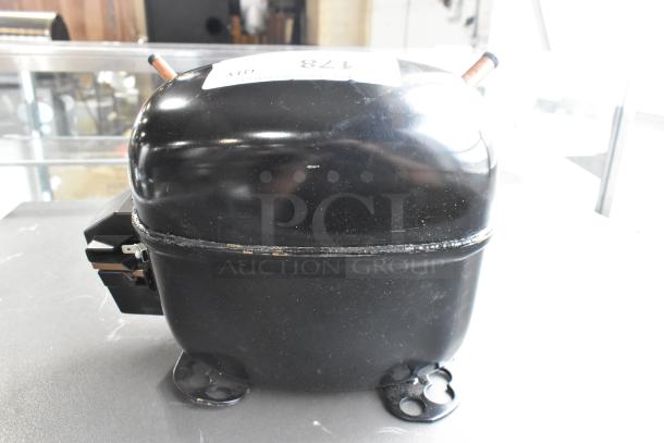 BRAND NEW SCRATCH AND DENT Secop SCE21CNLX motor, 115V, 1 phase, black casing, visible scratch on surface, sticker with item number.