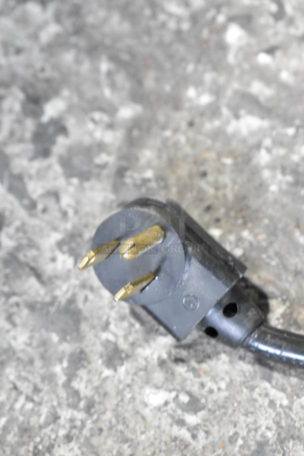 Close-up of a black three-prong plug for a metal commercial freezer, showing moderate wear and suitable for 115 volts, 1 phase.