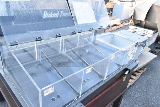 Clear dry display merchandiser with multiple poly bins, hinged lids, and visible pricing labels, suitable for baked goods.