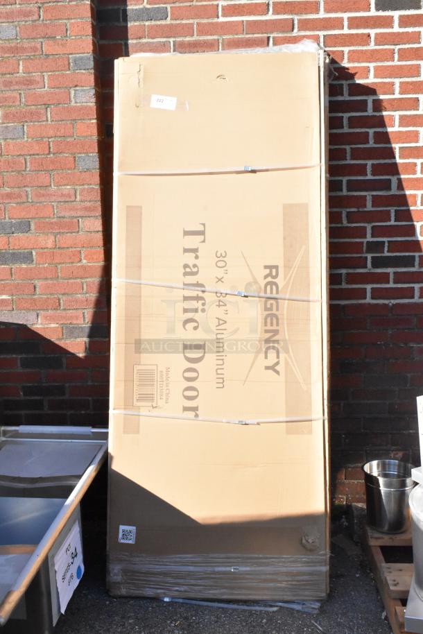 Two brand new Regency aluminum swinging traffic doors, 30" x 84", with a 9" x 14" window, in original packaging.