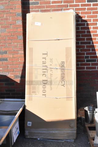 Two brand new Regency aluminum swinging traffic doors, 30" x 84", with a 9" x 14" window, in original packaging.