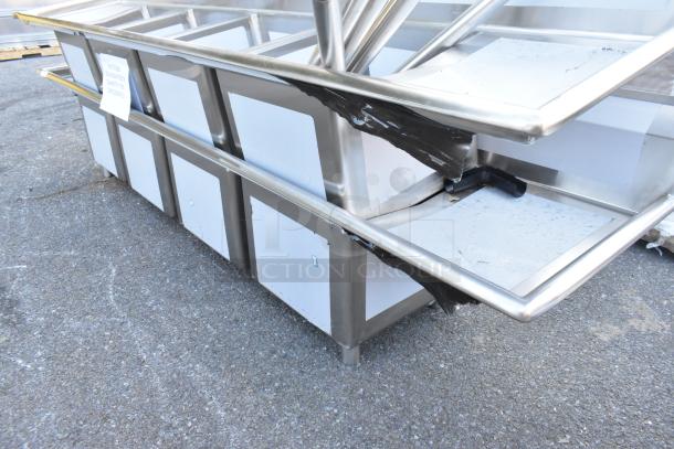Brand new Regency 600S41818218 stainless steel four compartment commercial sink with two drainboards, no legs, visible scratches and dents.