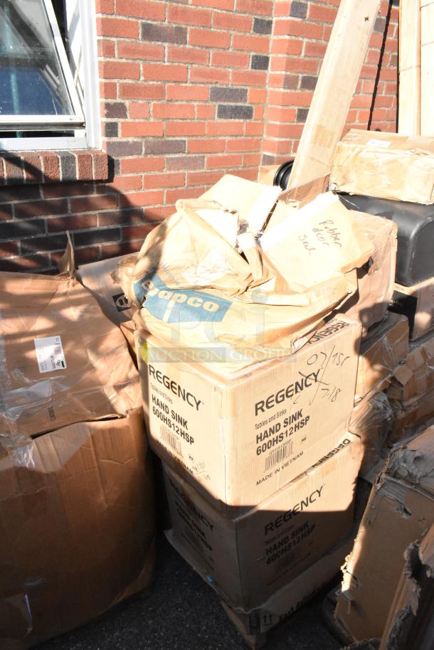 Stack of distressed boxes labeled "Regency Hand Sink 600HS12HSP" outdoors, sunlight casting shadows.