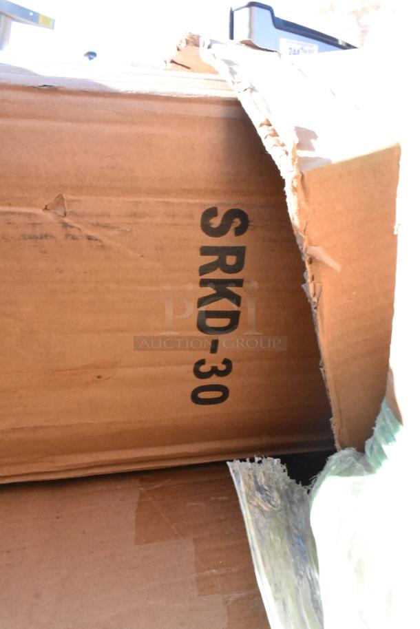 Damaged box labeled SRKD-30 containing scratch and dent items, including Steelton hand sinks and Regency ice and mop sinks.