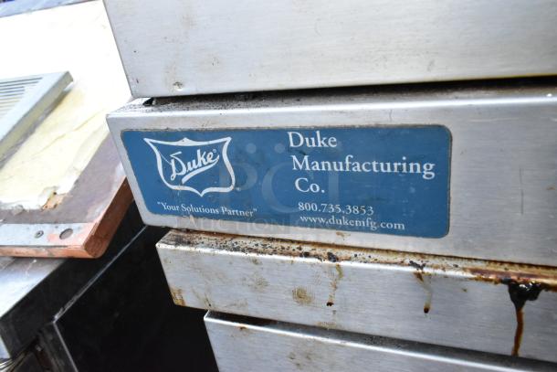 2 Duke stainless steel convection ovens, full size, view-through doors, metal racks, thermostatic controls, visible Duke label.