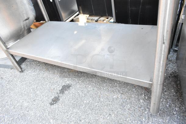 Stainless steel table with under shelf, sturdy metal construction, shows light wear, ideal for commercial or kitchen use.