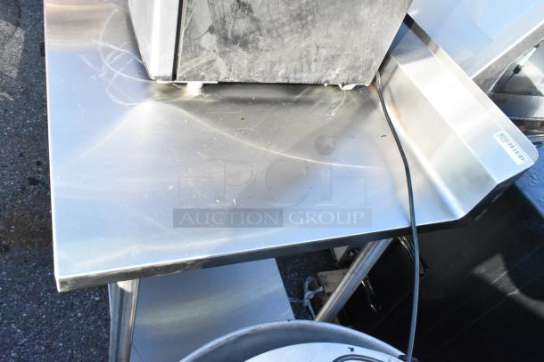 Stainless steel table with metal under shelf, lightly scratched surface, visible barcode label on edge.