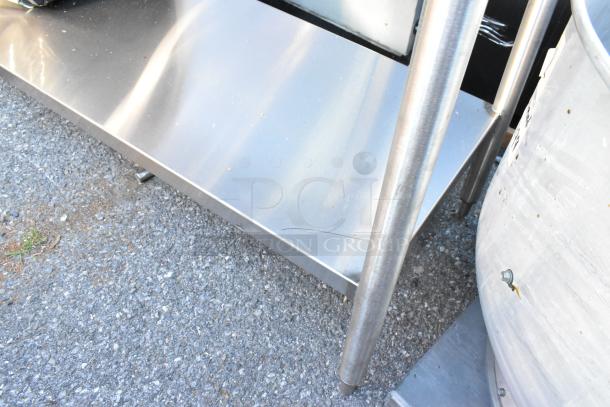 Stainless steel table with metal under shelf, sturdy legs, slight surface scratches. Great for industrial or kitchen use.