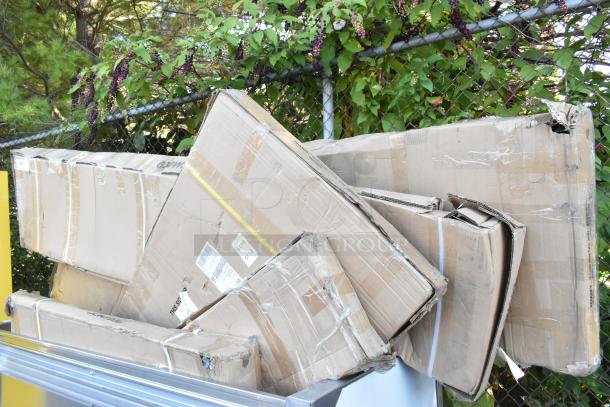 Stack of unopened boxes containing scratch and dent Regency stainless steel shelves and tables, visible packaging wear.