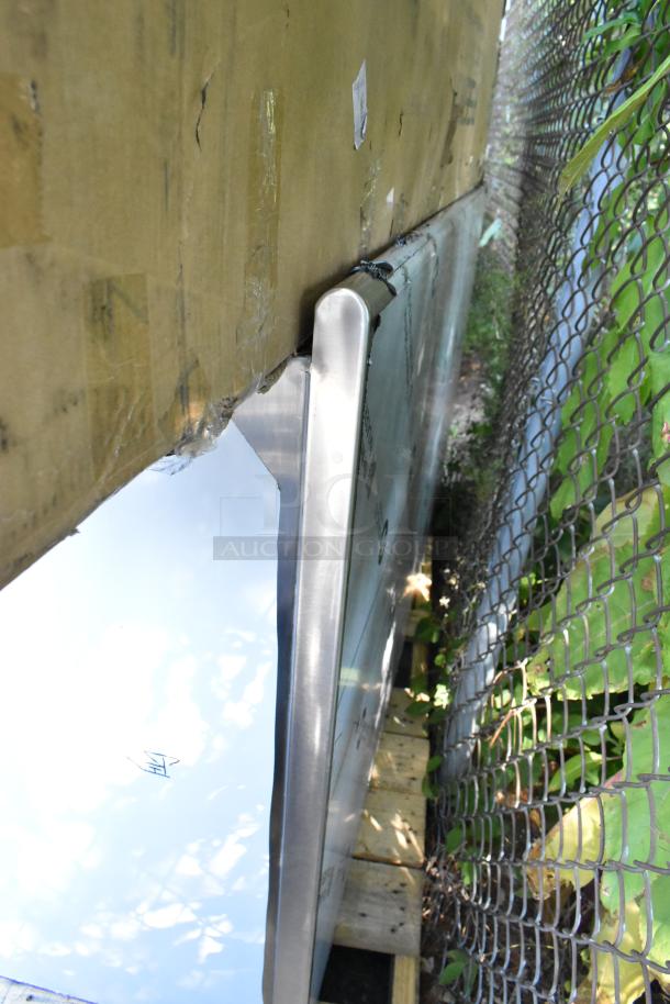 Brand new stainless steel counter, visible scratch and dent, against cardboard packaging, partially outdoors.