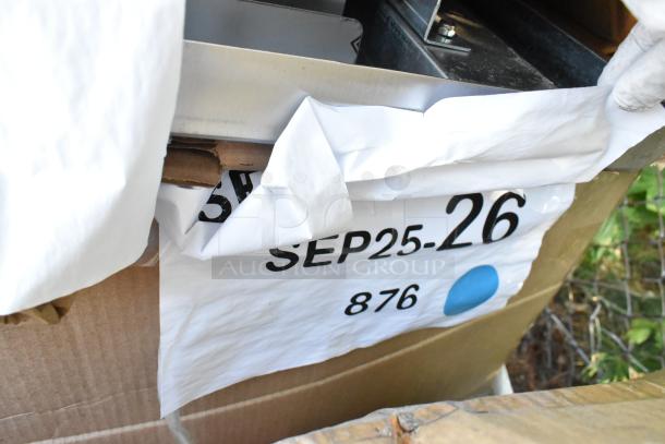 Box labeled "SEP25-26, 876" with visible scratch and dent on a partially unwrapped new furniture item, possibly a table or cabinet.