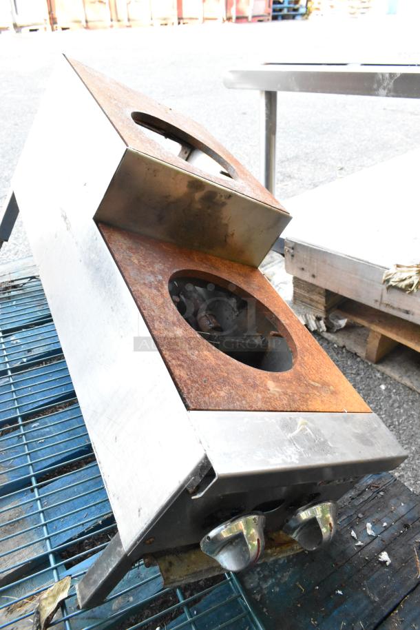 Metal Commercial Gas Powered 2 Tier 2 Burner Range, rusted surface, dual control knobs, outdoor setting, used condition.