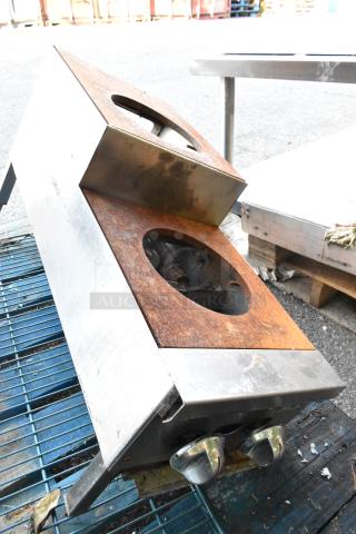 Metal Commercial Gas Powered 2 Tier 2 Burner Range, rusted surface, dual control knobs, outdoor setting, used condition.