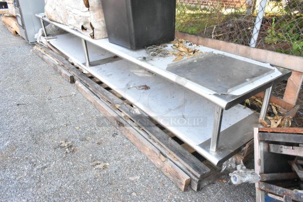 Regency 600PTSD24144 stainless steel pass-through shelf with overshelf, 24"x144", well-used, outdoor setting, holding items.