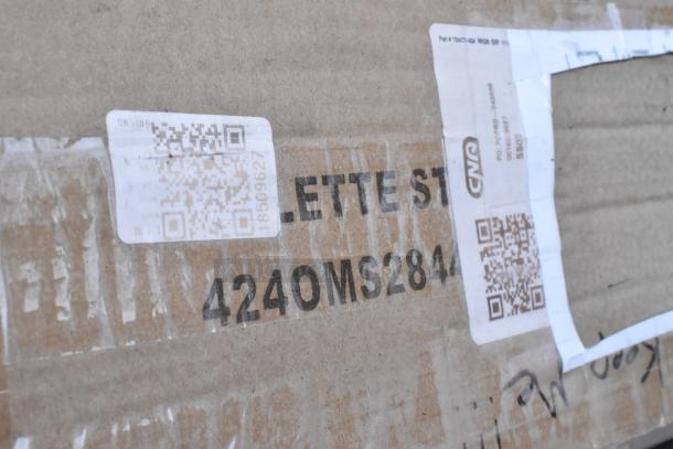 Cardboard box with shipping labels and QR codes, bearing the text "4240MS284." Part of a Seaga auction lot, new condition.