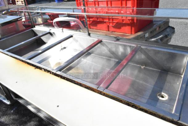 Stainless steel commercial steam table with sneeze guard, under shelf, used condition, visible wear on edges.
