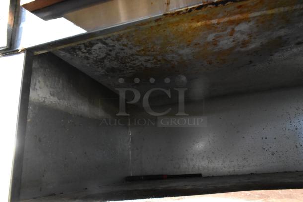 Stainless steel steam table with sneeze guard and under shelf, showing signs of wear, suitable for commercial use.