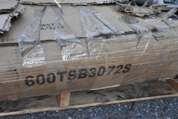 Cardboard box labeled "600TSB3072S" on a pallet, indicating new umbrella base and work table inside.