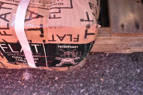 Cardboard box labeled "FLAT" with model FBT2093A01, sealed with white straps, resting on wooden pallet.