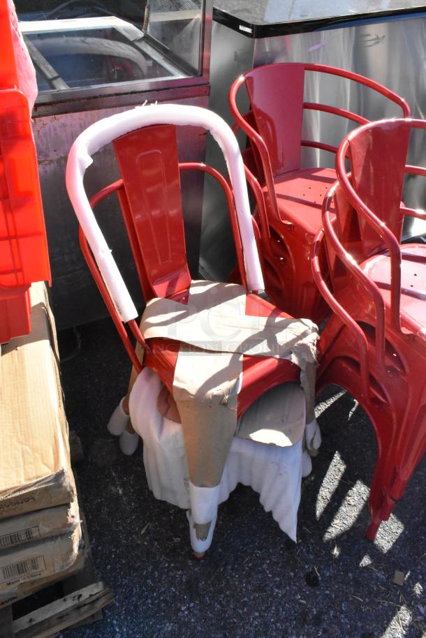 Eight brand new red Tolix style metal chairs, three with armrests, partially wrapped in protective material.