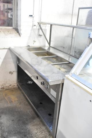 Stainless steel steam table with sneeze guard and under shelf. Features multiple compartments and control knobs. Moderate wear.