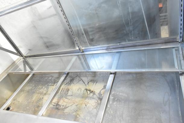 Stainless steel steam table with sneeze guard and under shelf, showing slight surface wear. Suitable for food service.