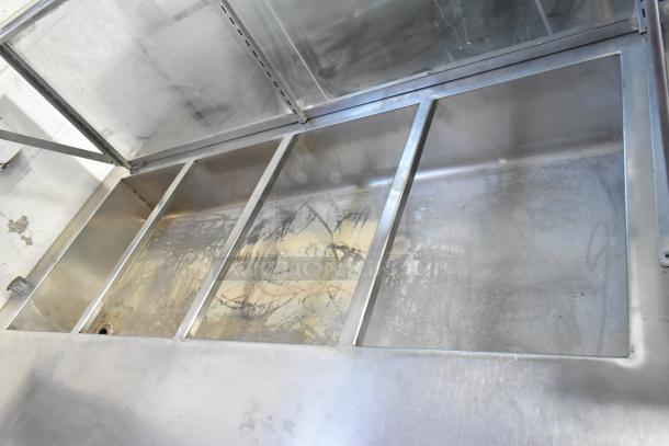 Stainless steel steam table with sneeze guard, four compartments, and under shelf, showing signs of wear.